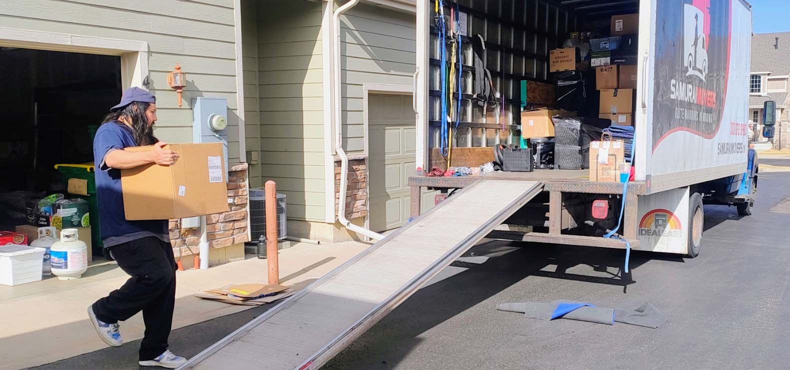 Mover carrying a packed box to a loaded Samurai Movers truck