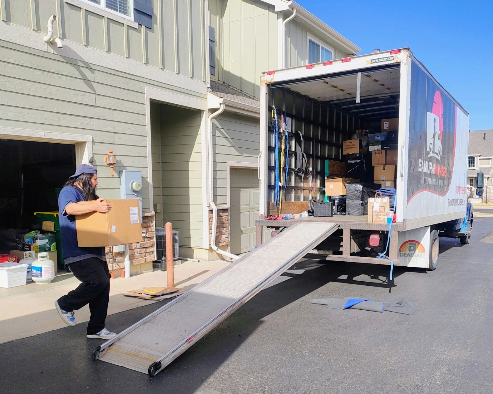 Mover loading boxes into a moving truck with a ramp in front of a house.