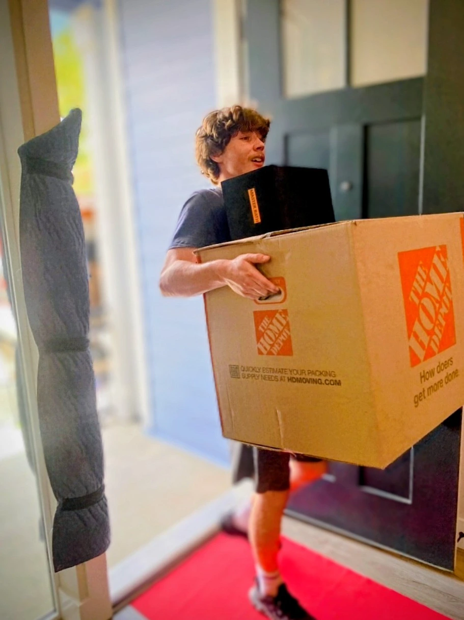 Young boy carrying a large box with Home Depot logo at the door.
