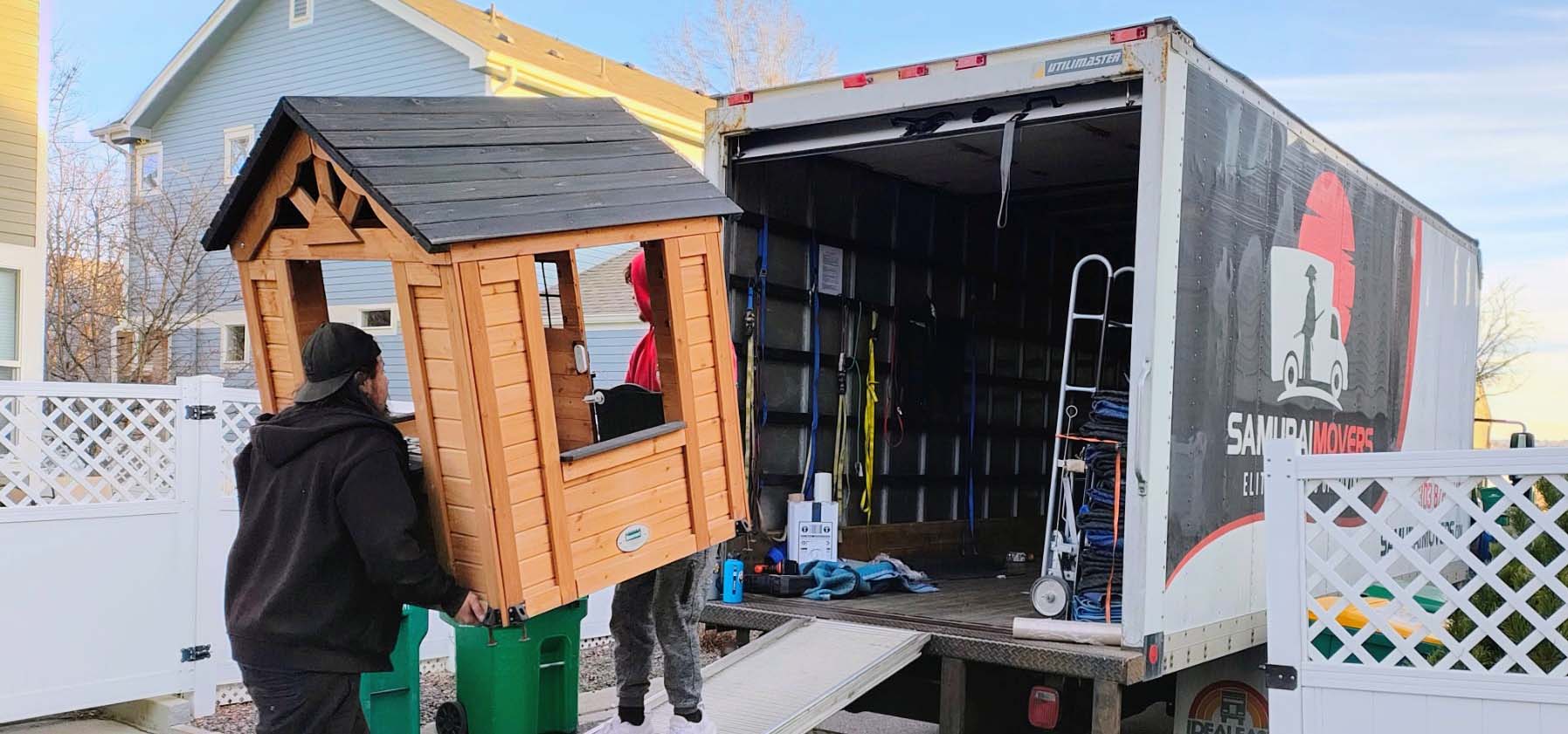 Movers loading a wooden playhouse onto a moving truck ramp