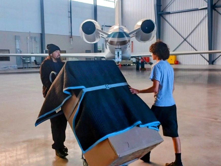 Movers carrying a blanket-wrapped item through an aircraft hangar during a commercial move