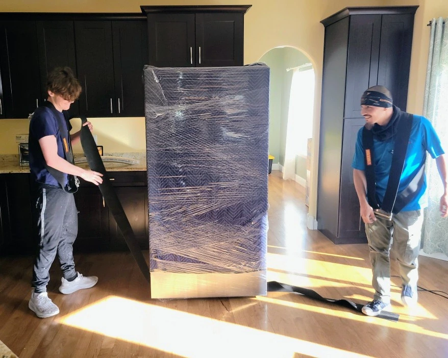 Movers shrink-wrapping a tall cabinet before a specialty item move